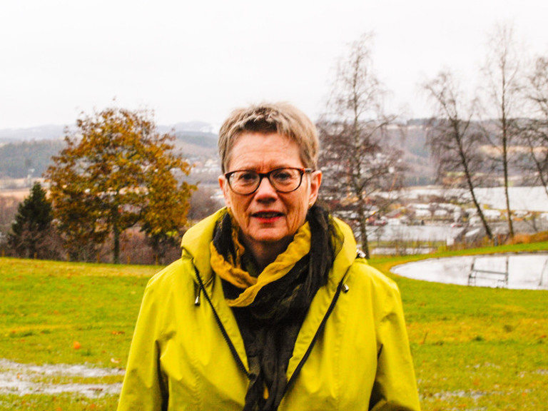 En kvinne i gul jakke står på en åker.